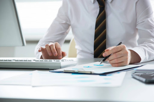 A businessman in a white button-down shirt and tie reviews performance numbers in an office; preparing a strategy for asset protection.